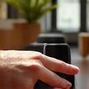An elderly hand wearing a smartwatch, which displays a fall detection alert on its screen, set in a comfortable home environment.